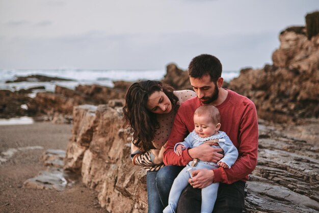 Retrato de una familia tradicional en una playa donde el padre y la madre abrazan a su bebé con Copyspace