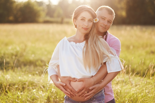 Retrato familiar al aire libre: hermosa joven embarazada y su esposo