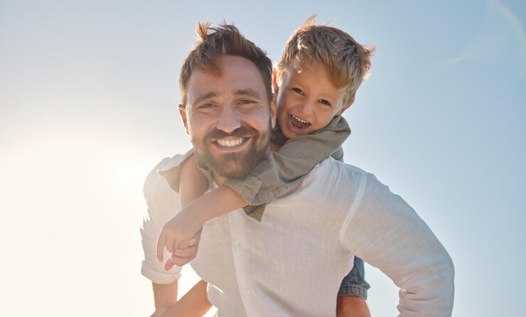 Retrato familiar y padre e hijo se relajan contra un fondo de cielo azul jugando y divirtiéndose al aire libre Feliz viaje familiar y niño abrazando a papá en la naturaleza riendo y disfrutando el verano juntos