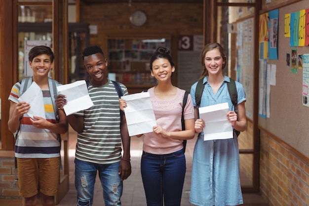 Retrato de felices compañeros sosteniendo tarjetas de grado en el corredor