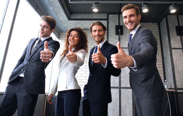 Retrato de felices empresarios de pie en la oficina mostrando el pulgar hacia arriba.