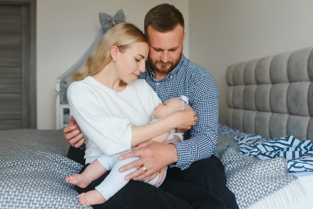 Retrato de felices padres jóvenes con bebé en la cama en casa