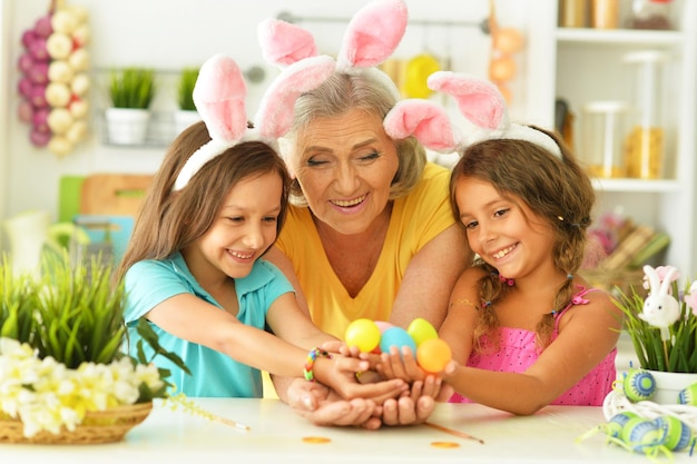 Retrato de feliz abuela y nietas coloreando huevos de Pascua