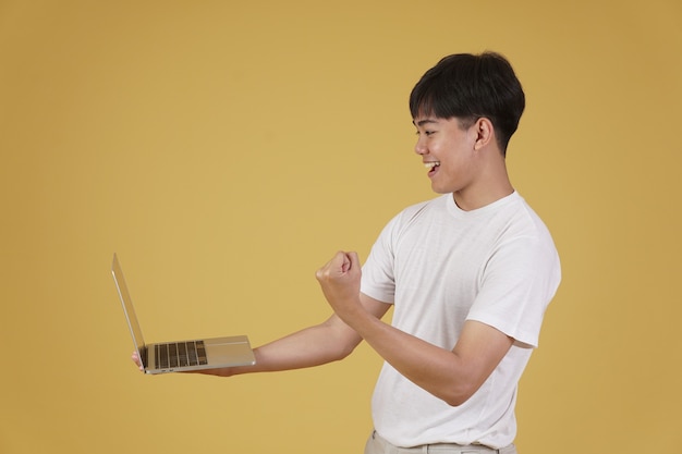Retrato de feliz alegre regocijo alegre joven asiático vestido casualmente sosteniendo la computadora portátil haciendo el gesto ganador del puño aislado