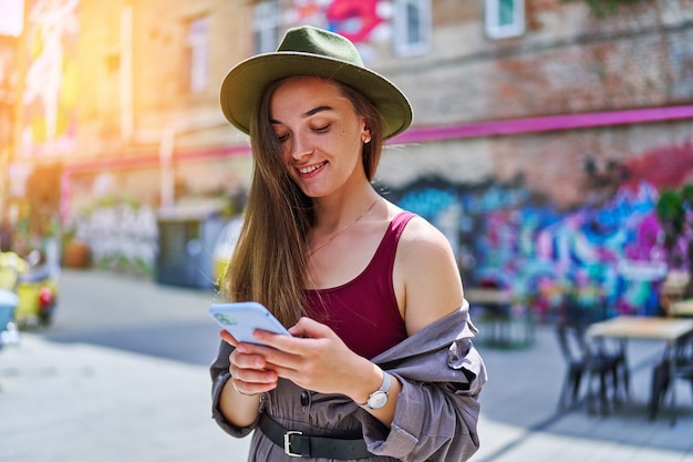 Retrato de feliz alegre sonriente hermosa linda joven milenaria alegre usando teléfono al aire libre