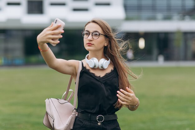 Retrato de una feliz alegre sonriente joven estudiante colegiala dama con cabello largo con anteojos tomar una selfie.