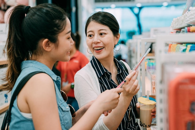 retrato feliz amigas asiáticas están discutiendo los bolígrafos que eligen mientras compran juntos en una papelería brillante durante las vacaciones de verano.