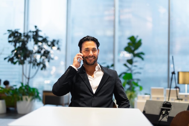 Foto retrato de feliz apuesto hombre de negocios hispano en la cafetería sonriendo y hablando por teléfono