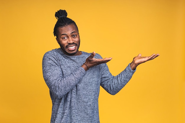 Retrato de feliz apuesto joven afroamericano con una sonrisa casual, apuntando a un lado con el dedo, con expresión de la cara emocionada aislada sobre fondo amarillo.