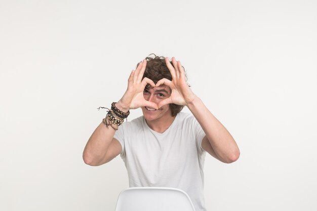 Retrato de feliz apuesto joven haciendo corazón con los dedos sobre fondo blanco.