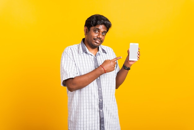 Retrato feliz asiático jovem negro sorri em pé vestindo camisa fazendo dedo apontando na tela em branco do celular digital inteligente isolada, fundo amarelo com espaço de cópia
