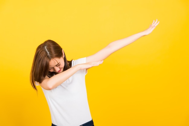 Retrato feliz asiático linda jovem bonita sorriso adolescente em pé vestindo camiseta movendo mostrando dança DAB contra gesto isolado, estúdio filmado em fundo amarelo com espaço de cópia