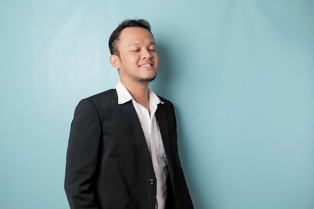 Un retrato de un feliz y atractivo hombre asiático sonríe con traje aislado por un fondo azul