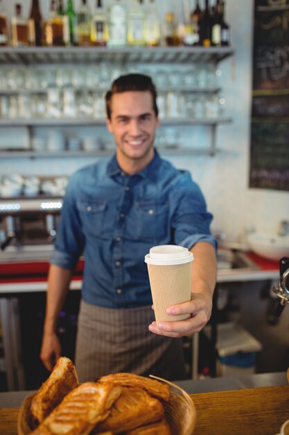 Retrato de feliz barista ofreciendo café en vaso desechable en cafe