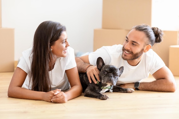 Retrato feliz casal multiétnico se unindo com cachorro em casa nova