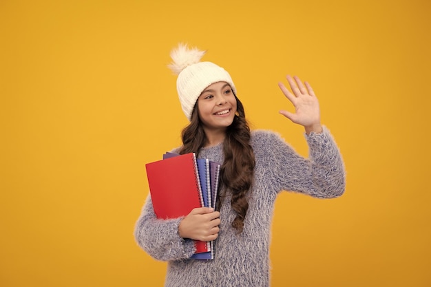 Foto retrato de una feliz colegiala adolescente de 12 13 14 años con gorro de punto y suéter cálido con mochila sobre fondo amarillo