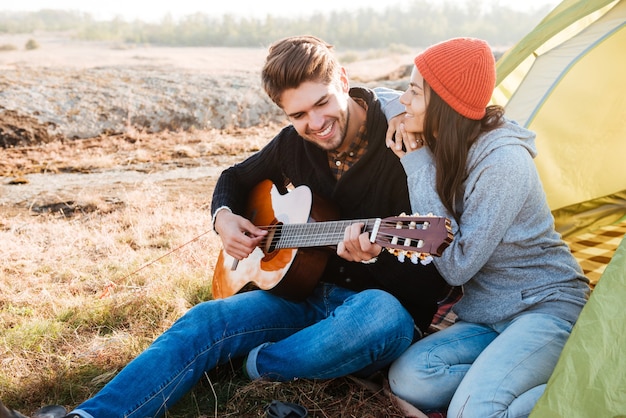 Retrato de un feliz couople con guitarra habiendo acampar con carpa al aire libre