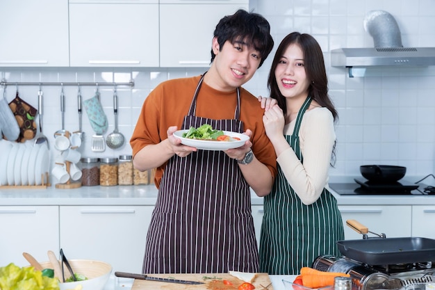 Retrato feliz de amar jovem asiático de se divertir de pé um alegre preparar comida e desfrutar de cozinhar