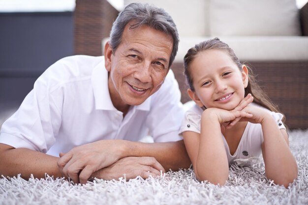 Retrato feliz e avô com a menina em casa de férias ou férias juntos na aposentadoria com sorriso Homem idoso e avô relaxam com a criança no chão na sala de estar e se unem no México