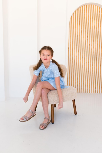 Retrato de una feliz y emocionada chica con un vestido azul liso en un interior claro