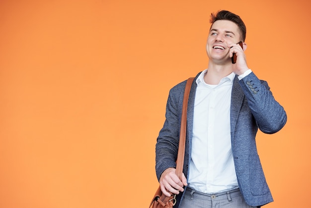 Retrato de feliz emocionado joven empresario hablando por teléfono con un compañero de trabajo, aislado en naranja