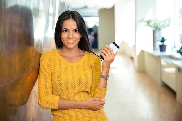 Retrato de una feliz empresaria casual sosteniendo smartphone en el pasillo