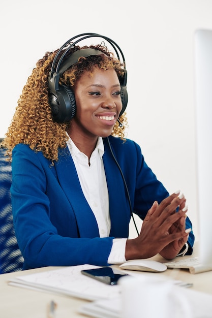 Retrato de feliz empresaria joven usando audífonos al tener una reunión en línea con colegas o socios comerciales