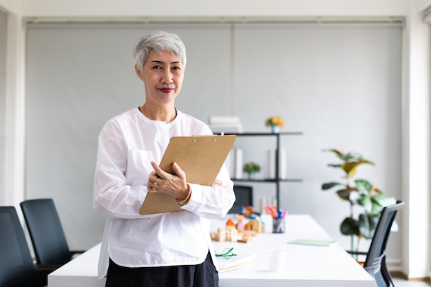 Retrato de feliz empresaria senior con anteojos mirando a cámara. Líder ejecutiva femenina de pelo gris de los 60.