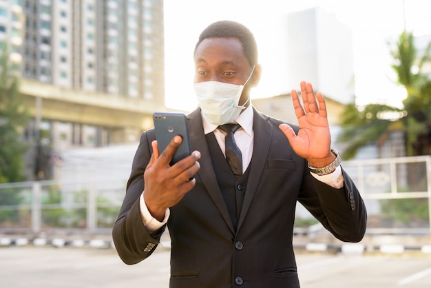 Retrato de feliz empresario africano con máscara de video llamada en las calles de la ciudad