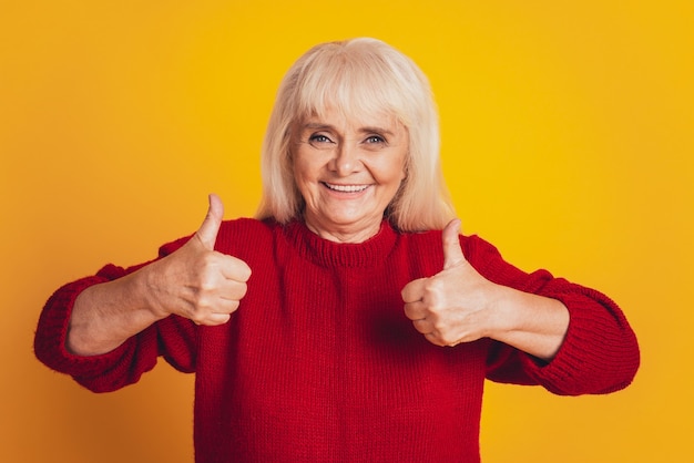 Retrato de feliz encantadora dama madura mostrando los dedos pulgar de acuerdo aislado sobre fondo amarillo