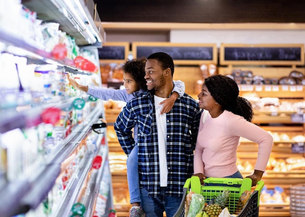 Retrato de una feliz familia negra con un carrito de compras juntos en la tienda de comestibles