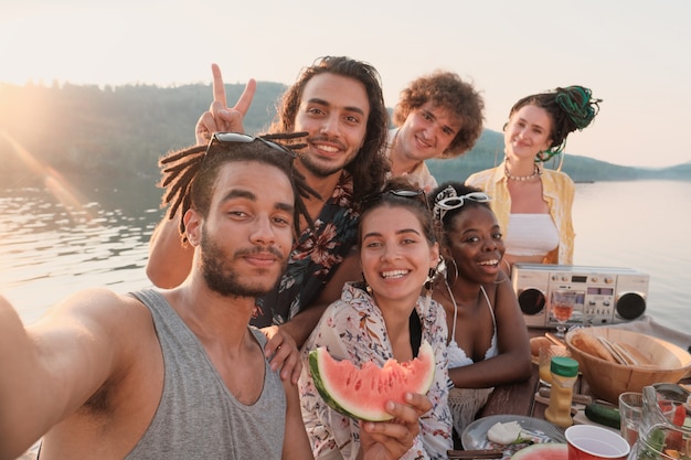 Retrato de feliz grupo de amigos sonriendo y posando a la cámara que hacen retrato selfie durante un picnic al aire libre
