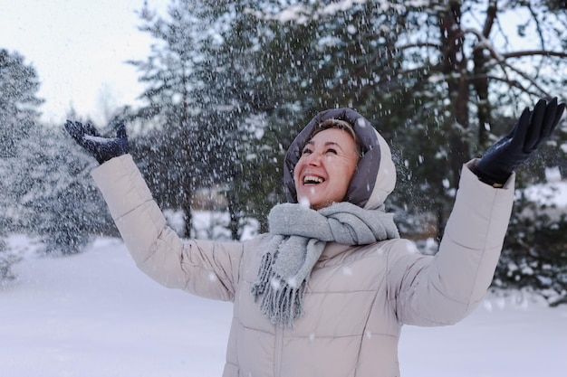 Retrato de feliz y hermosa anciana jubilada en edad está jugando a divertirse con la nieve al aire libre en el bosque o parque en el día frío de invierno sonriendo disfrutar del clima