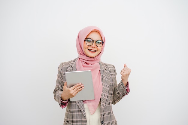 Foto retrato de una feliz y hermosa joven mujer de negocios musulmana con hiyab rosa. trabajadora de una compañía con gafas sonriendo y sosteniendo una tableta digital de pie sobre un fondo blanco.