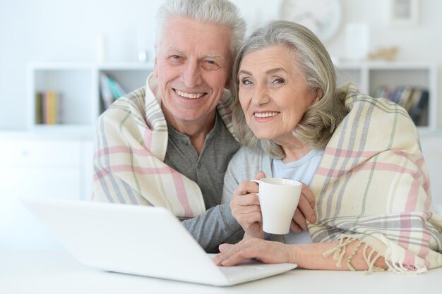 Retrato de una feliz y hermosa pareja de ancianos con una manta usando una laptop en casa