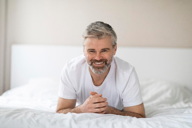 Retrato de feliz hombre de mediana edad acostado en la cama sonriendo