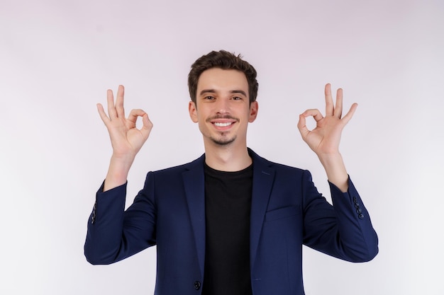 Retrato de feliz joven apuesto hombre de negocios haciendo bien firmar con la mano y los dedos sobre fondo blanco.