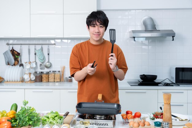 Retrato feliz de joven asiático de sentarse un alegre preparar comida y disfrutar de cocinar cocinar con verduras mientras está de pie en una cocina vida de condominio o casa