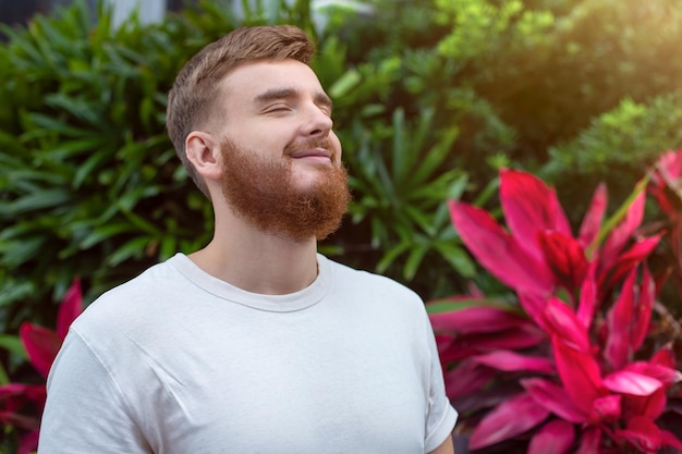 Retrato de feliz joven barbudo con barba respirando profundamente inhalar aire fresco sobre fondo natural