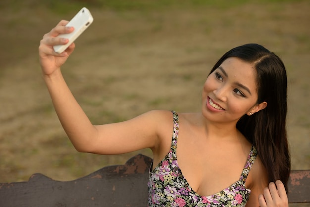 Retrato de feliz joven bella mujer asiática tomando selfie en el parque