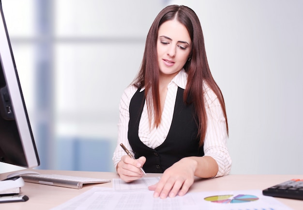 Retrato de feliz joven empresaria sentado en el escritorio calculando finanzas