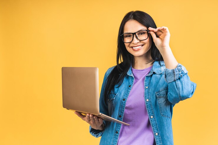 Foto retrato de feliz joven hermosa mujer sorprendida con gafas de pie con portátil aislado sobre fondo amarillo espacio para texto