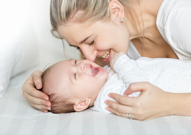 Retrato de feliz joven madre besando a su bebé en la cama