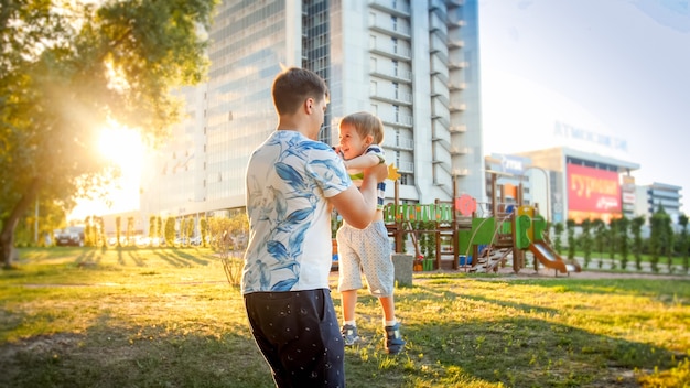 Retrato de feliz joven padre abrazando y girando a su pequeño hijo sonriente en el parque