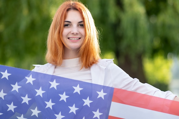 Retrato de feliz joven pelirroja sosteniendo la bandera nacional de EE. UU.