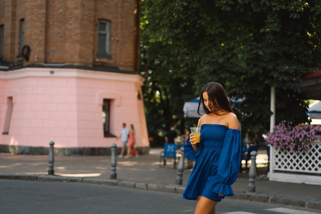 Retrato feliz joven vistiendo un vestido azul y bebiendo limonada cóctel de verano