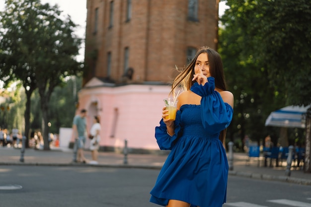 Retrato feliz joven vistiendo un vestido azul y bebiendo limonada cóctel de verano