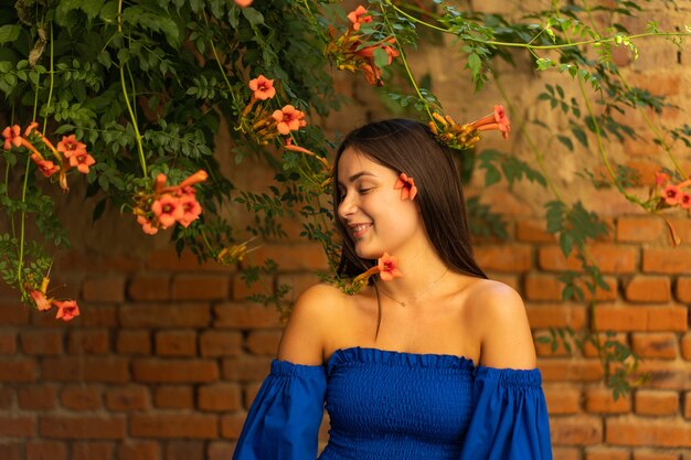 Foto retrato feliz joven vistiendo un vestido azul y de pie sobre campsis radicans flores