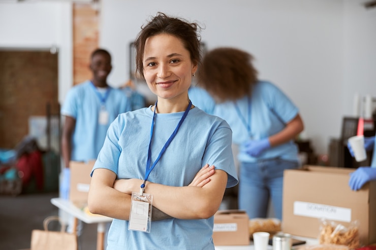 Foto retrato de feliz joven voluntario en uniforme azul sonriendo a la cámara mientras está de pie con los brazos
