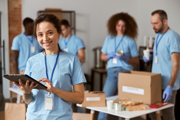 Retrato de feliz joven voluntario en uniforme azul con tablet pc y sonriendo a la cámara